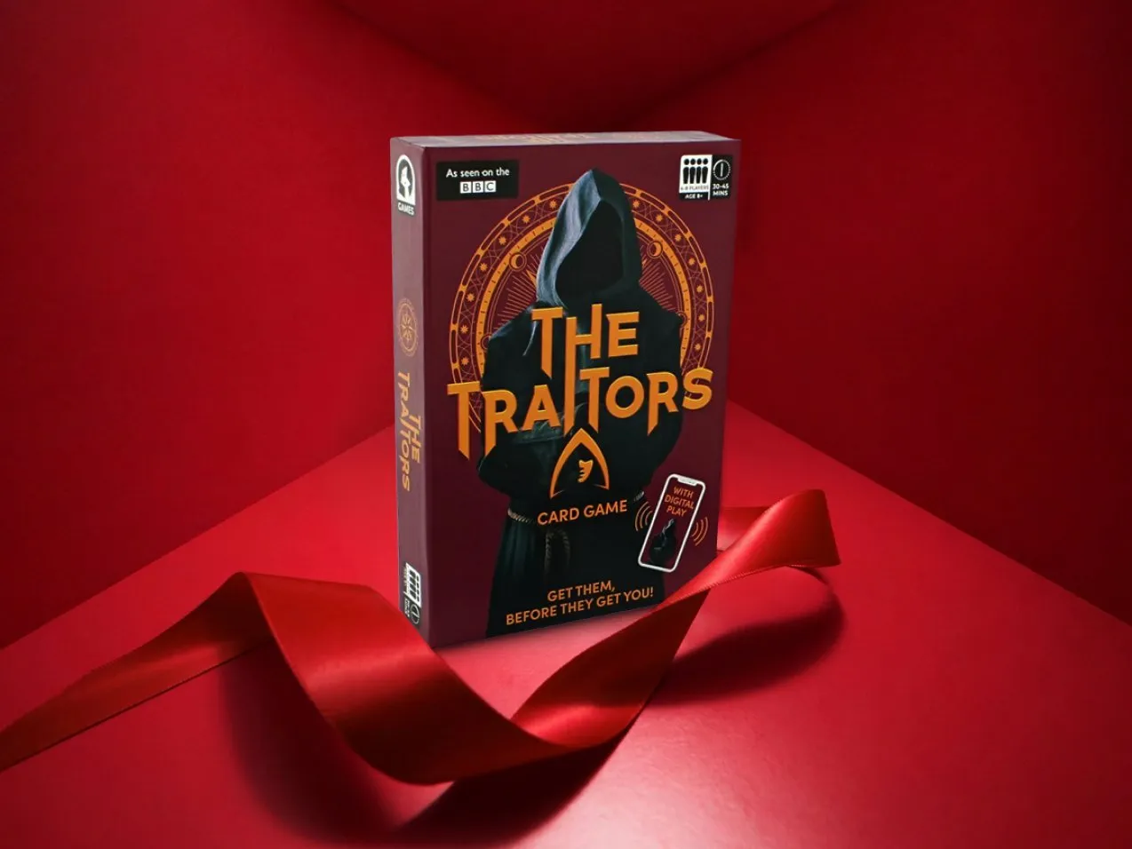 The Traitors card game box on a red background with ribbon, BBC branded party game gift idea for adults