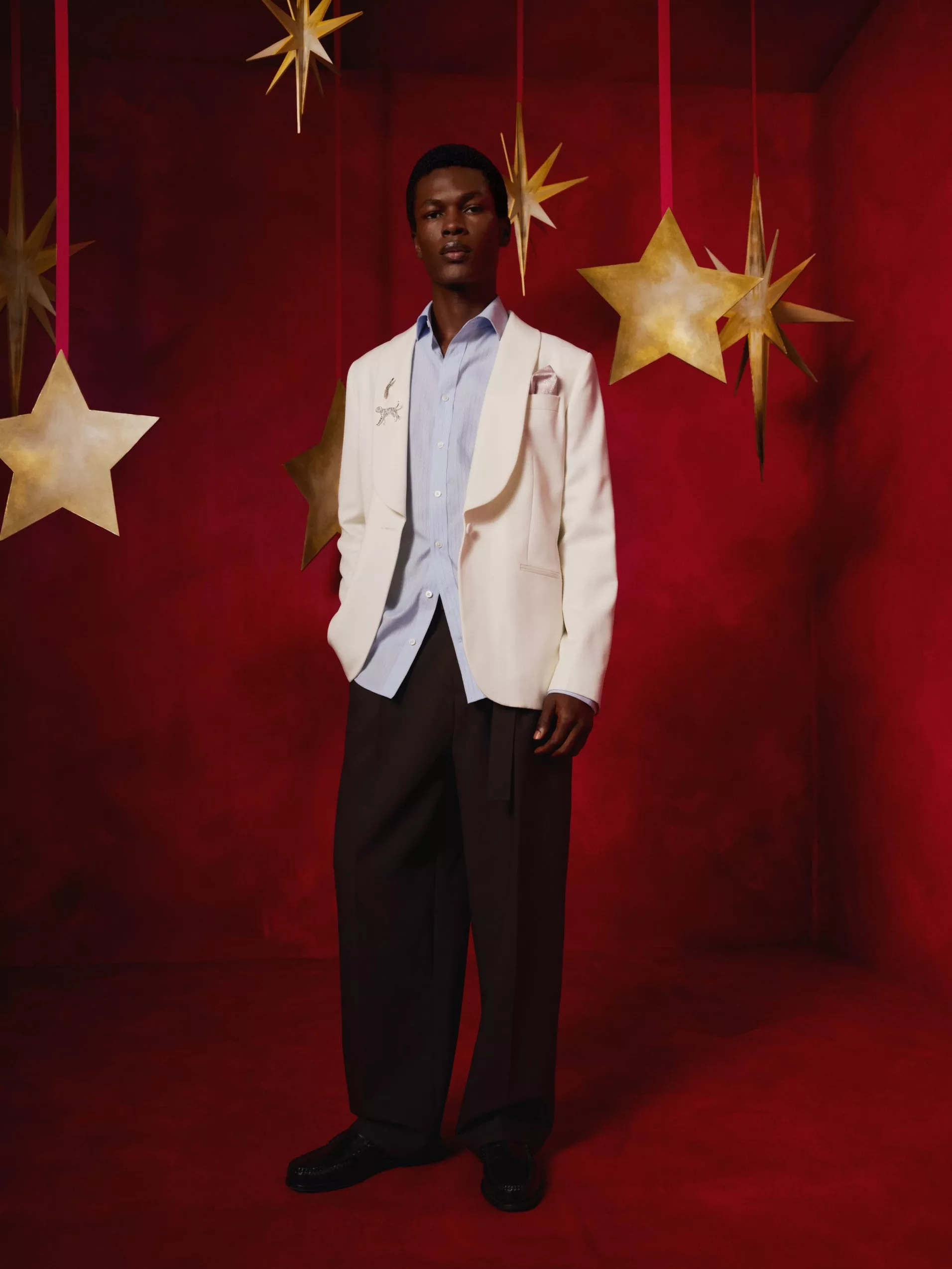 Fashion portrait of man in ivory blazer and blue shirt, on red studio set with hanging gold stars decor