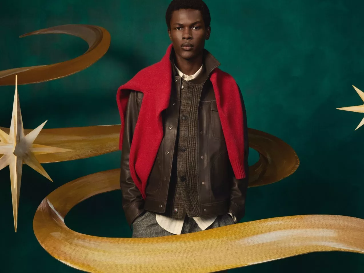 Fashion editorial portrait of male model in leather jacket and red scarf with gold ribbon backdrop