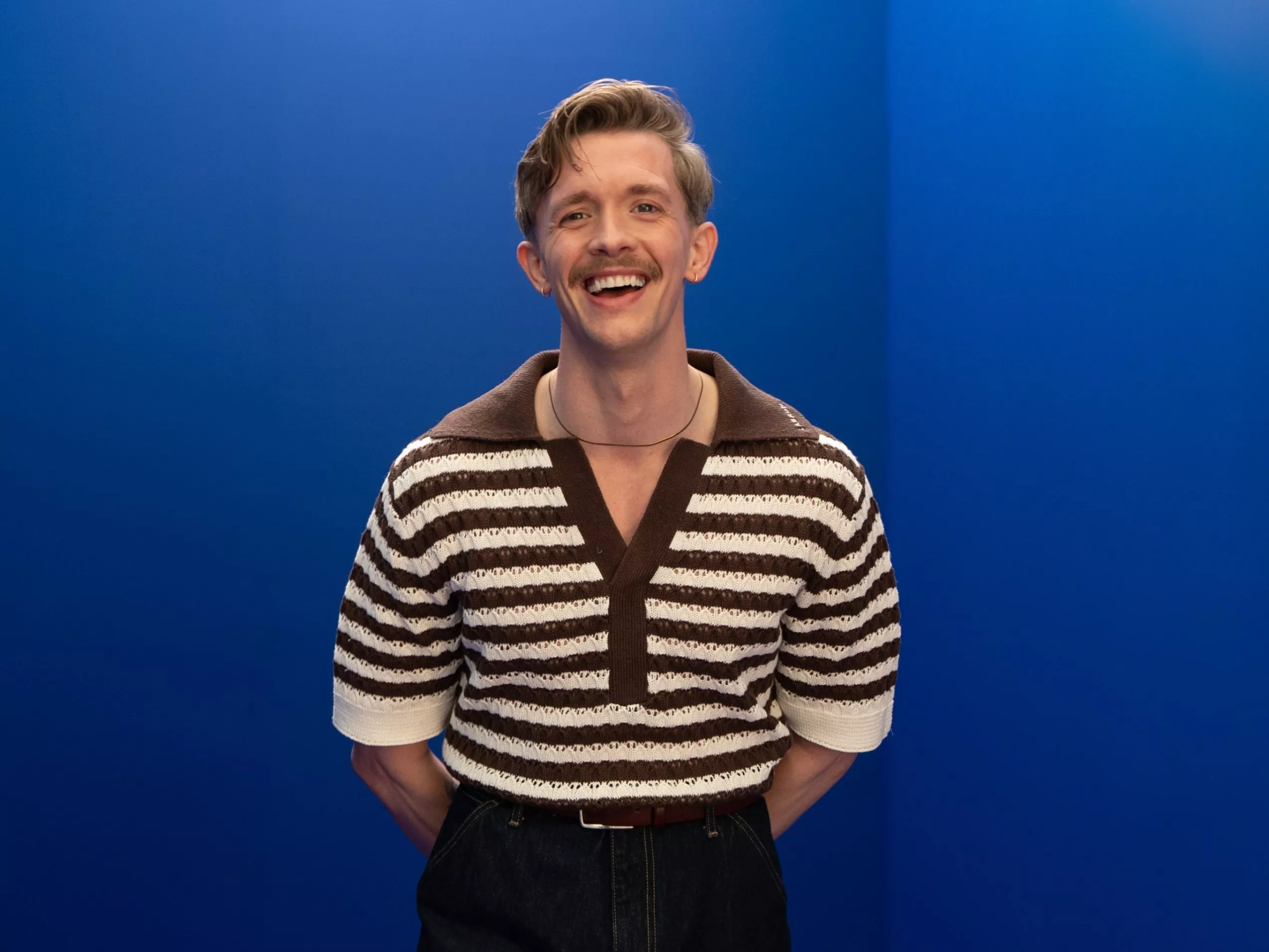 Smiling man in brown and cream striped knit polo shirt, studio portrait against bright blue background