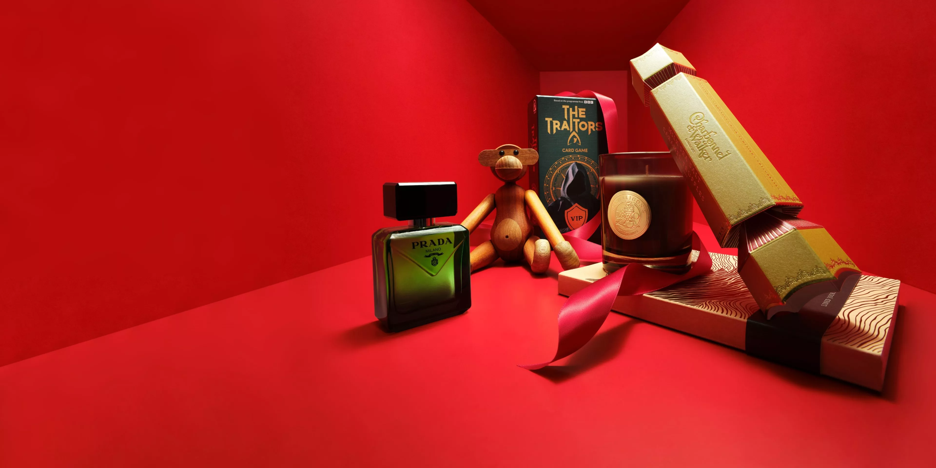 Luxury gift hamper on red background with Prada fragrance, candle, card game, wooden toy and boxed crackers ribbon