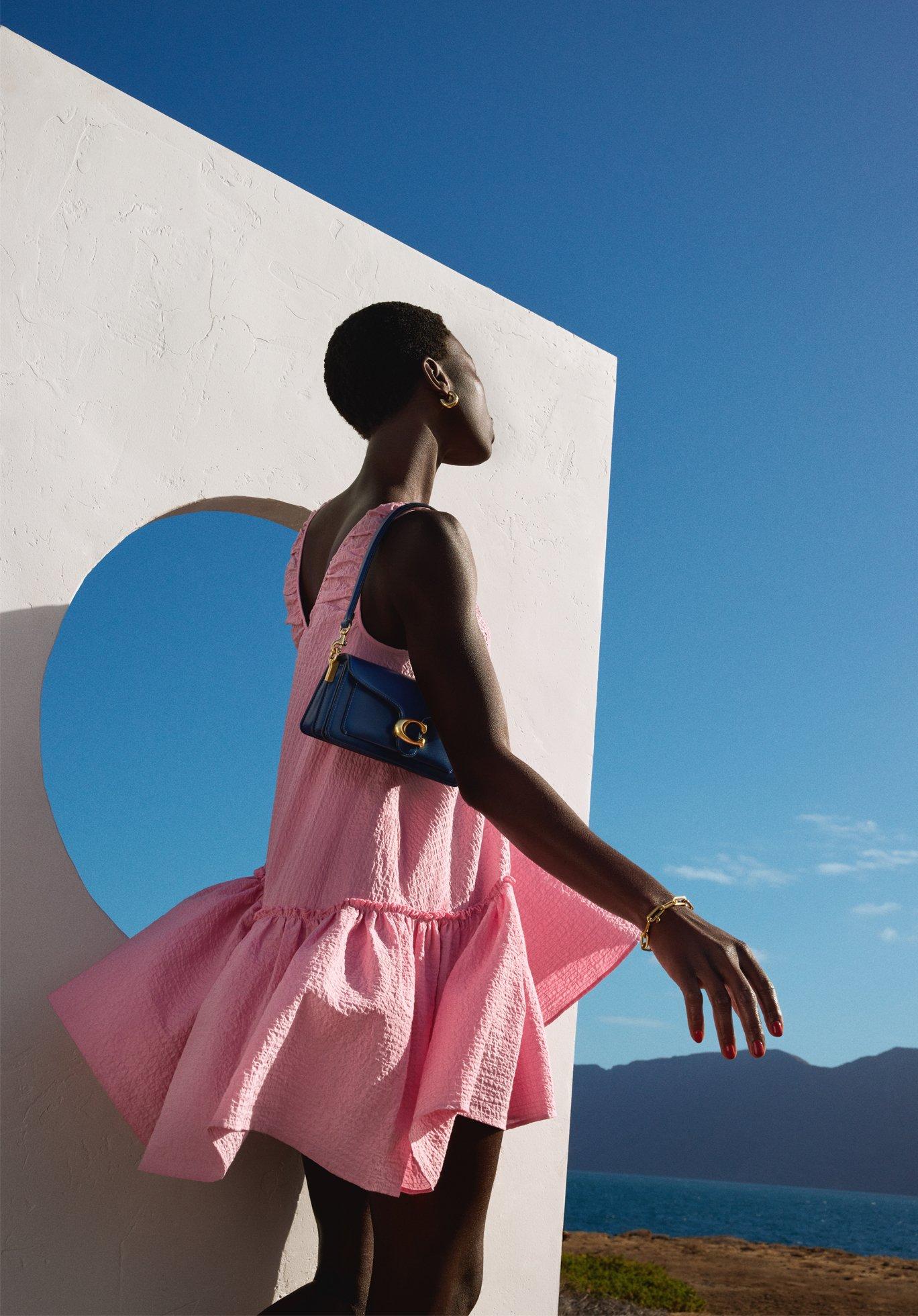 Image of a model wearing a pink dress, a white structure behind her and blue sky